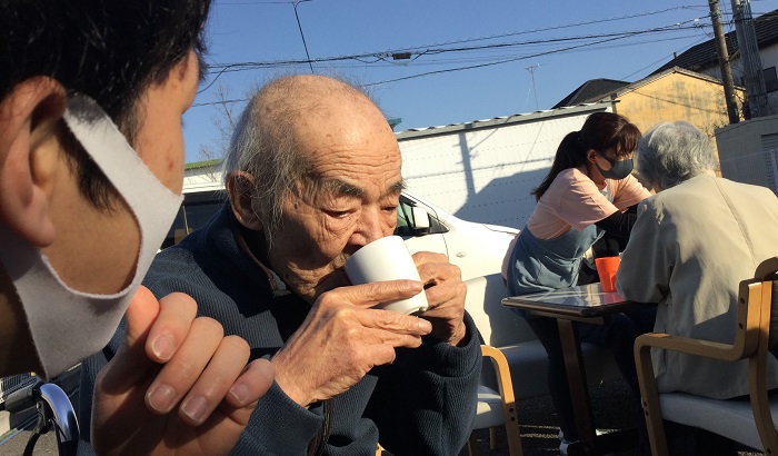 お外でお茶を召し上がるご利用者さまと見守るスタッフ